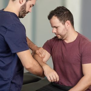 A physical therapist performs an elbow exercise on a patient.